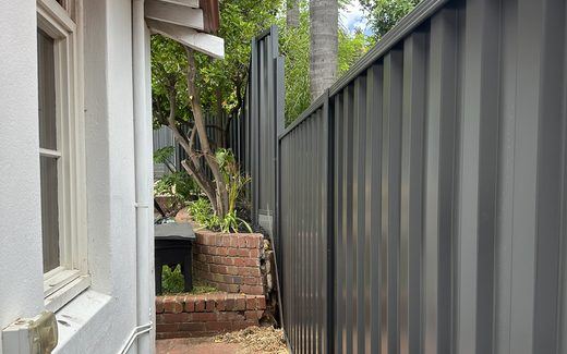 Colorbond fence running beside a narrow brick side path