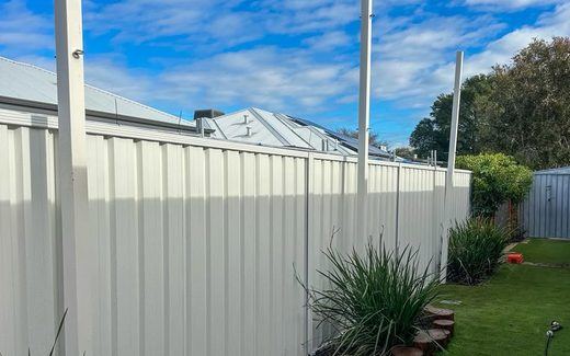Cream Colorbond fence behind a planted garden bed and lawn