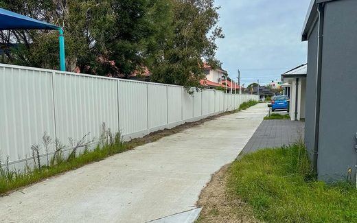 Cream Colorbond fence running beside a concrete pathway between homes