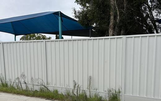 Cream Colorbond fence beside a backyard with a blue shade sail