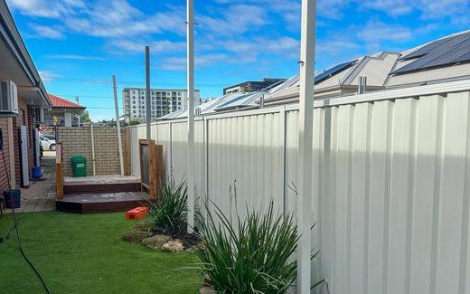 Cream Colorbond fence along a side yard with artificial turf and garden edging