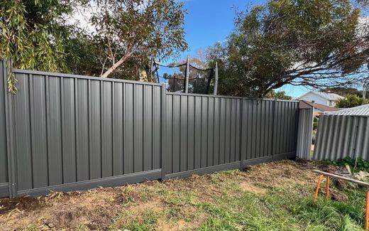 Long run of grey Colorbond fencing along a rear boundary under gum trees