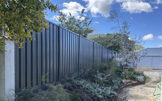 Monument Colorbond fence behind a landscaped garden bed under a blue sky