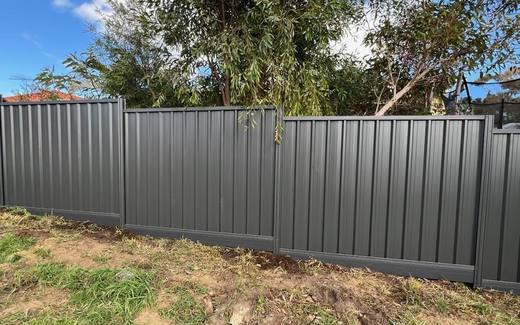 Long run of monument Colorbond fencing along a rear boundary under a blue sky