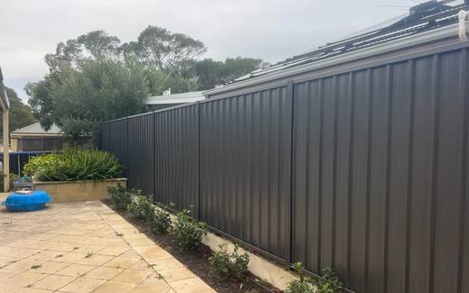 Monument Colorbond fence beside a paved courtyard and garden bed