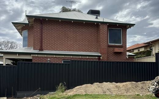 Dark Colorbond rear boundary fence with a brick home behind