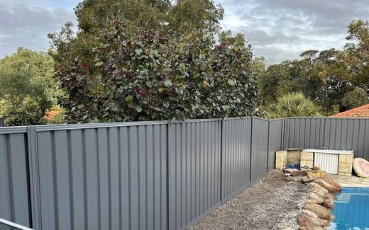 Grey Colorbond fence running behind a pool with rock edging and established trees