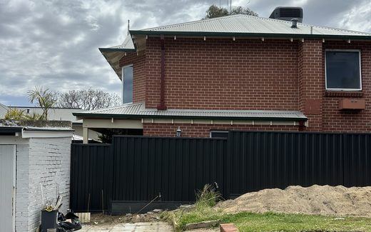 Colorbond fencing stepped along a brick retaining wall beside a garden