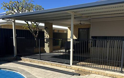 Black tubular pool fence enclosing a covered pool beside an alfresco area