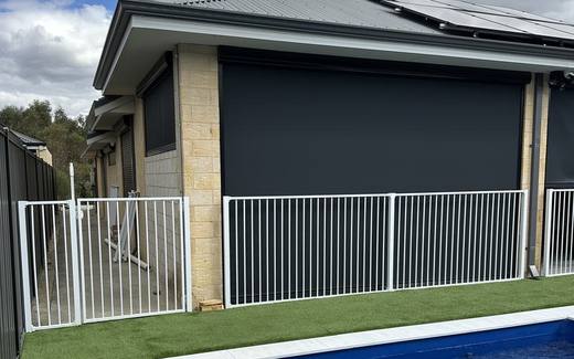 White tubular pool fence along the edge of a pool with artificial lawn