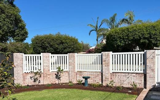 White picket fence between rendered brick piers with lawn and garden