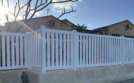 White PVC picket fence built on top of a limestone retaining wall