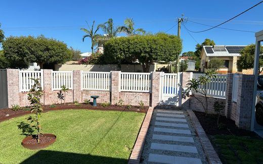 White PVC picket fence on brick piers along a freshly laid front lawn