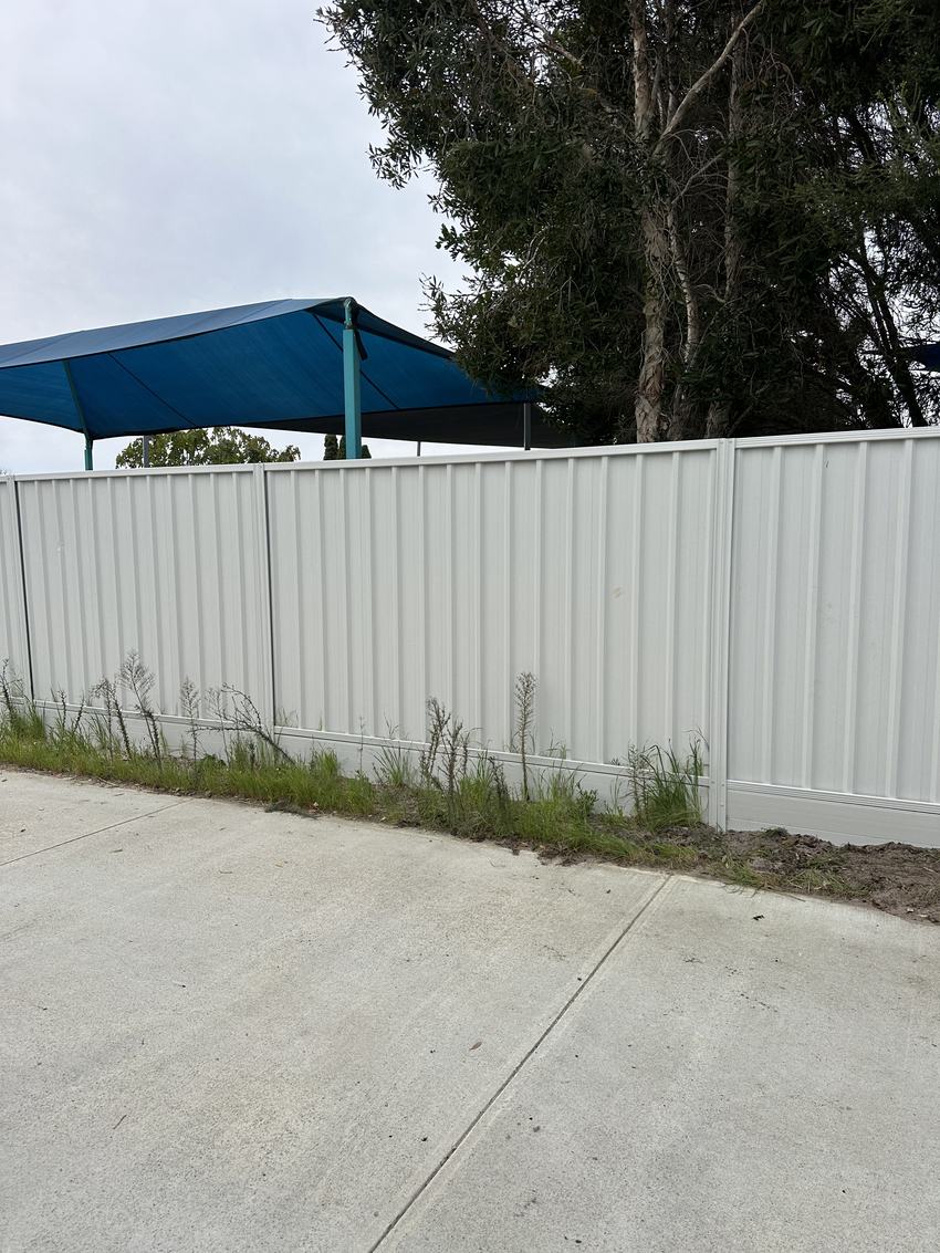 Cream Colorbond fence beside a backyard with a blue shade sail