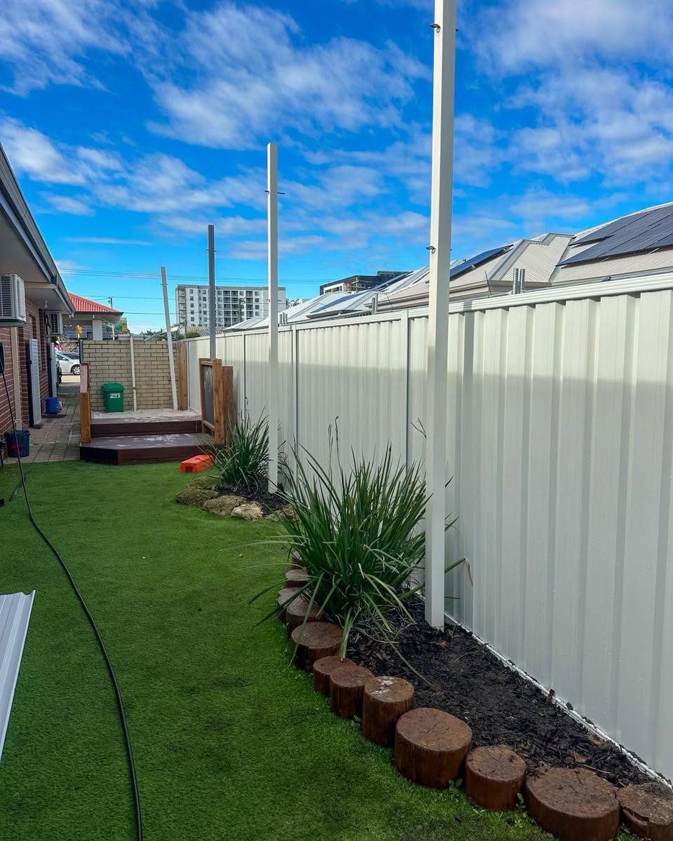 Cream Colorbond fence along a side yard with artificial turf and garden edging