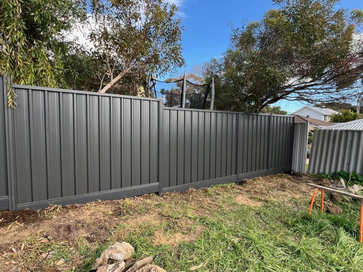 Long run of grey Colorbond fencing along a rear boundary under gum trees
