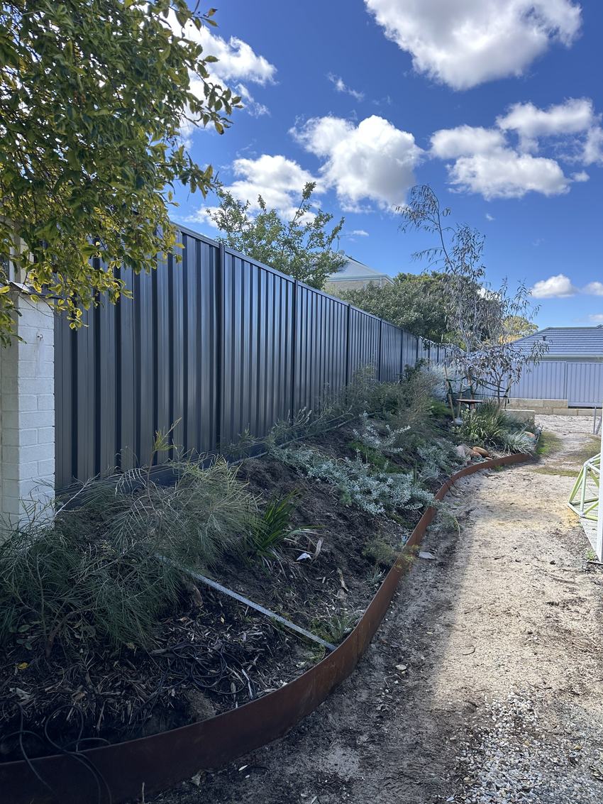 Monument Colorbond fence behind a landscaped garden bed under a blue sky