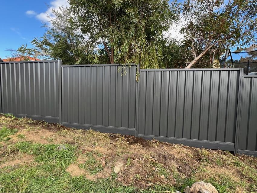Long run of monument Colorbond fencing along a rear boundary under a blue sky