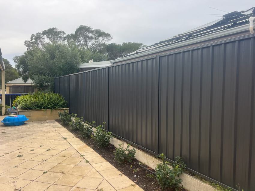 Monument Colorbond fence beside a paved courtyard and garden bed