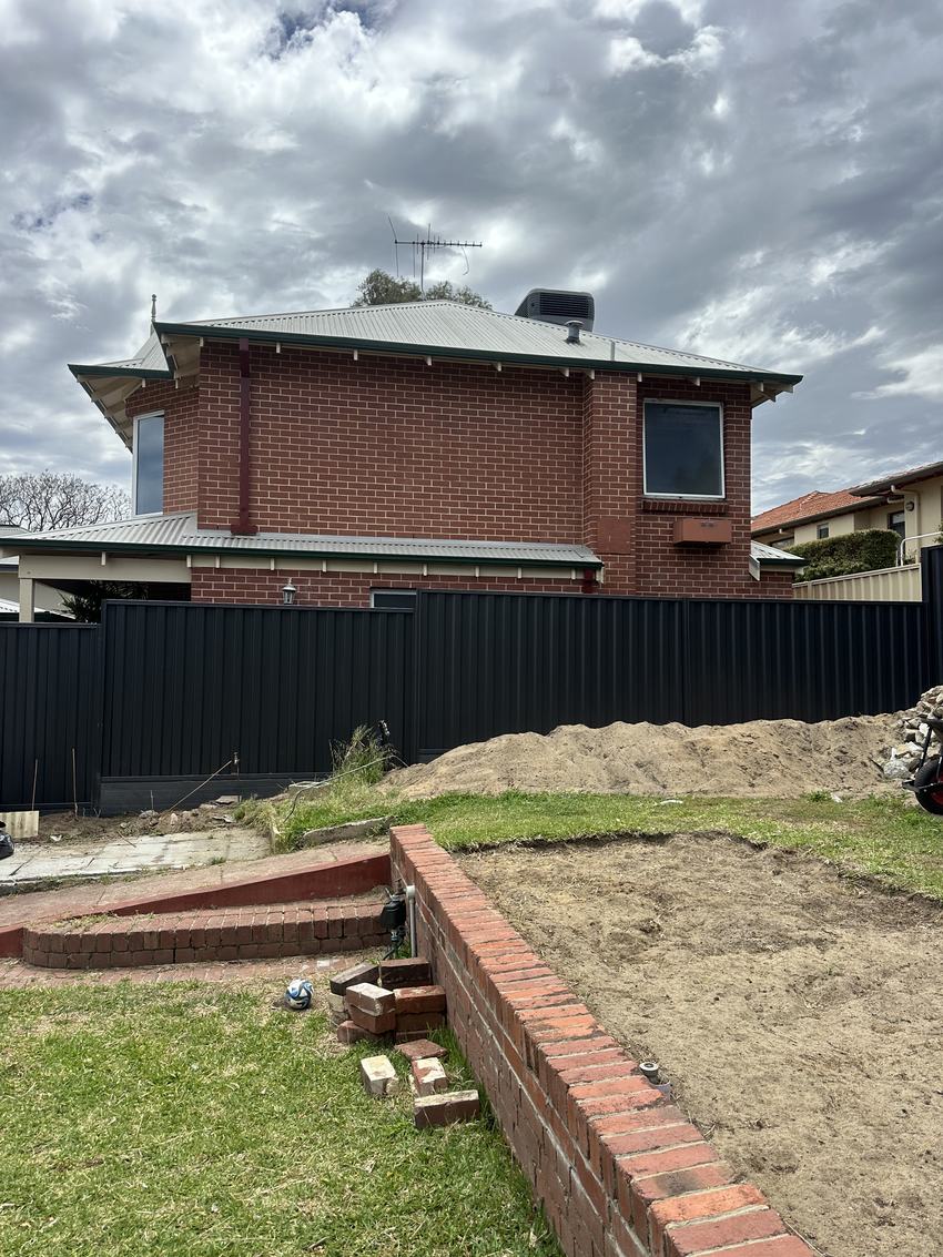 Dark Colorbond rear boundary fence with a brick home behind