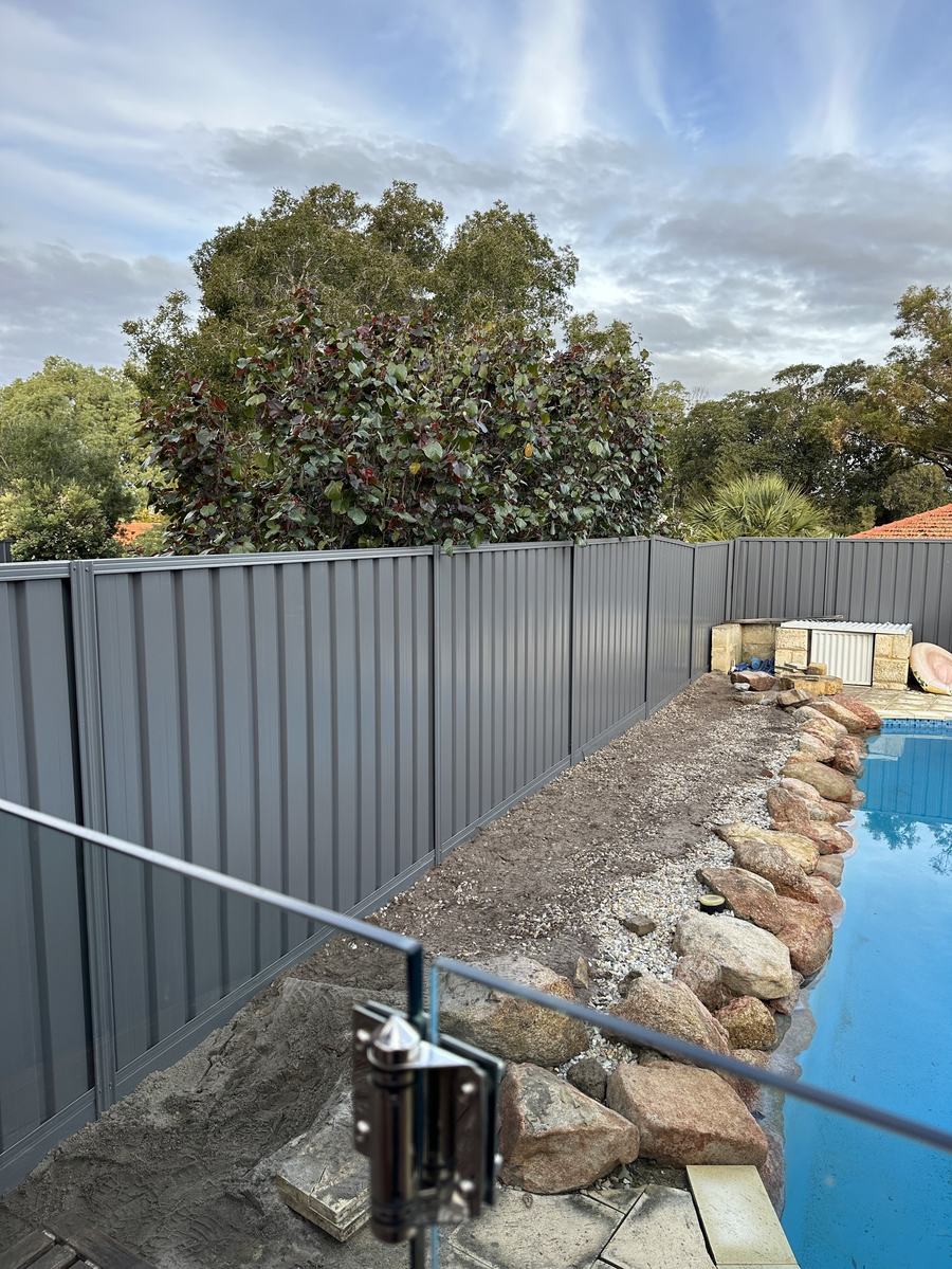 Grey Colorbond fence running behind a pool with rock edging and established trees