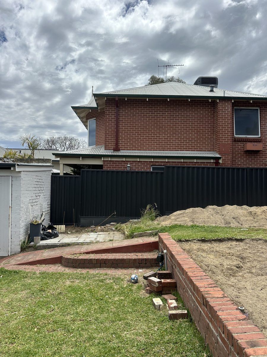 Colorbond fencing stepped along a brick retaining wall beside a garden
