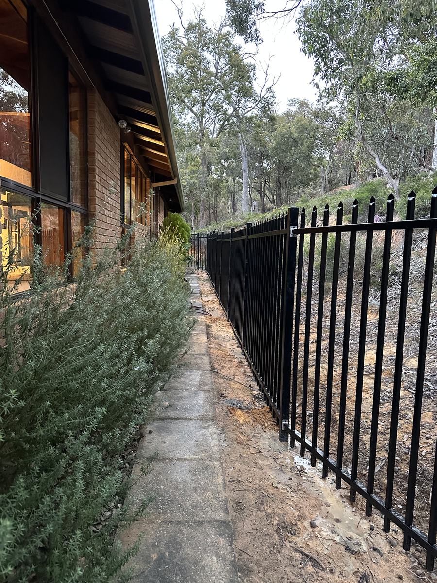 Black garrison spear-top security fence running along a path beside a home