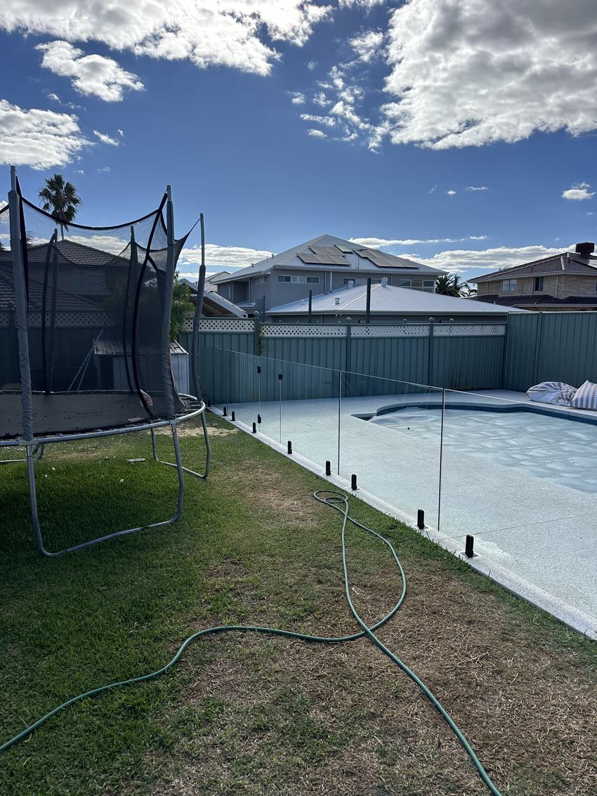 Frameless glass pool fence separating a pool from a backyard lawn