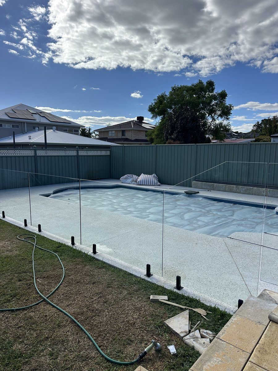 Frameless glass pool fence beside a pool and lawn under a cloudy sky