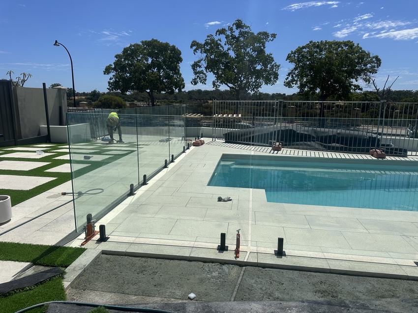 Wide view of a frameless glass pool fence enclosing a large pool and paved surround