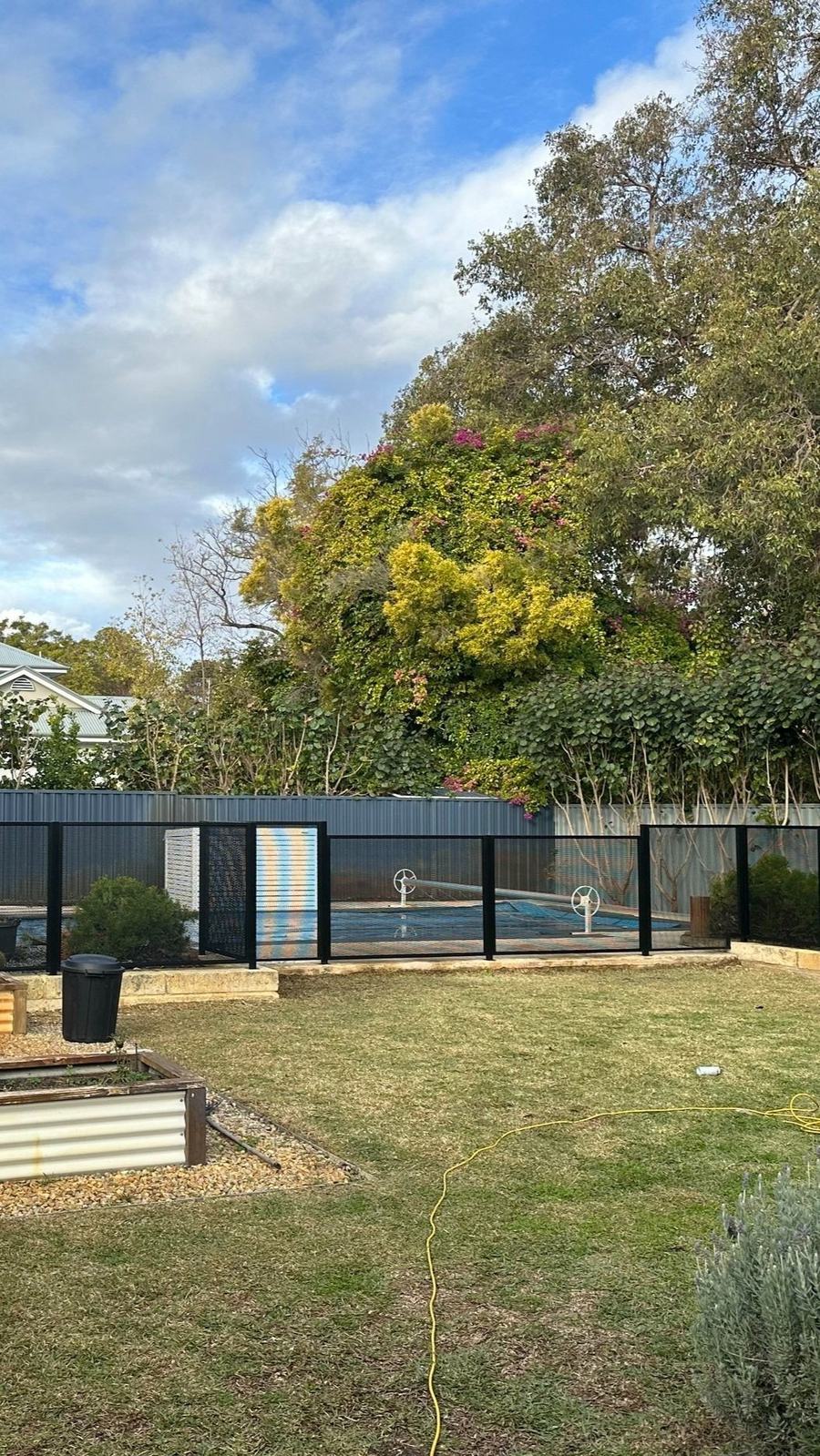 Black perforated panel pool fence and gate enclosing a pool, seen across a back lawn