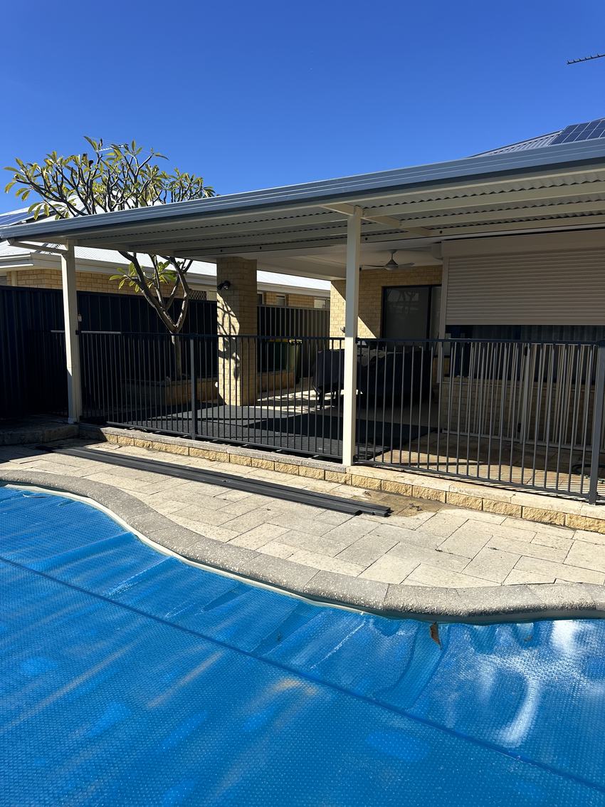 Black tubular pool fence enclosing a covered pool beside an alfresco area