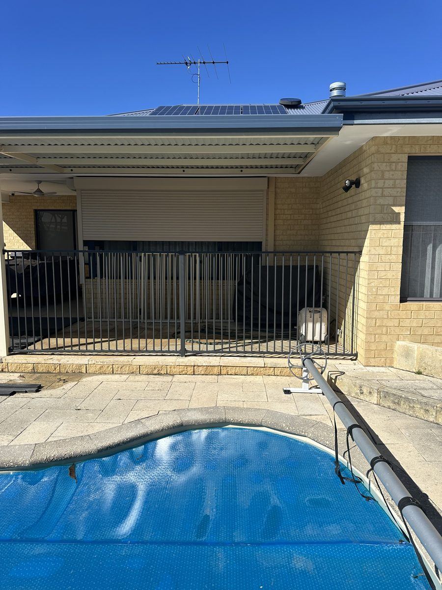 Black tubular pool fencing around a pool with brick paving and patio