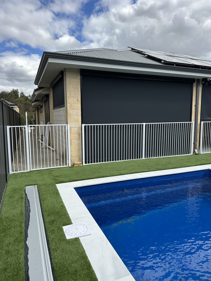 White tubular pool fence along the edge of a pool with artificial lawn