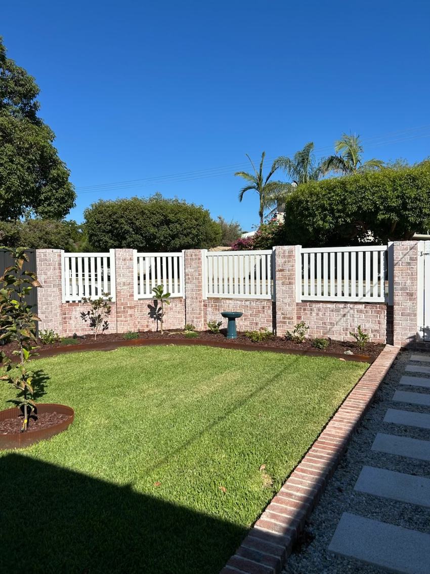 White picket fence between rendered brick piers with lawn and garden