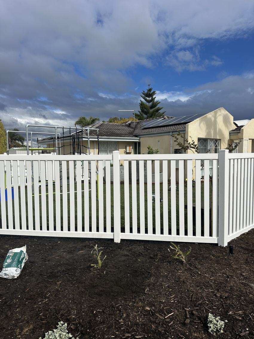 White PVC picket fence behind a freshly planted garden bed