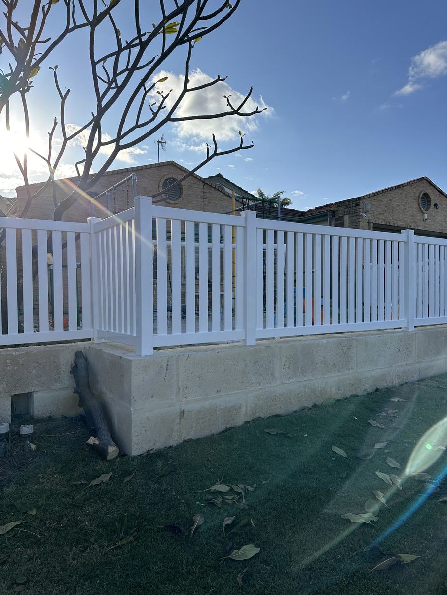 White picket fence built on top of a limestone wall against a blue sky