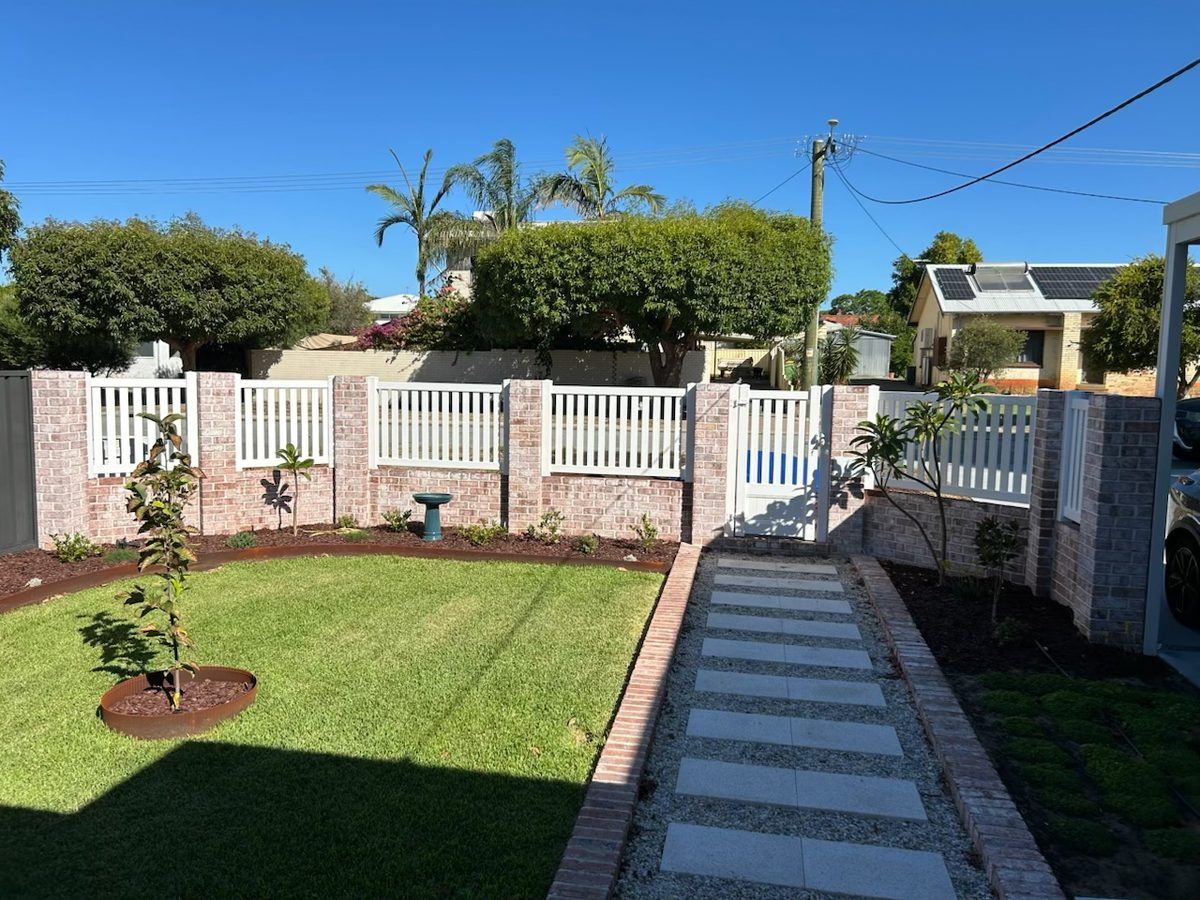 White PVC picket fence on brick piers along a freshly laid front lawn
