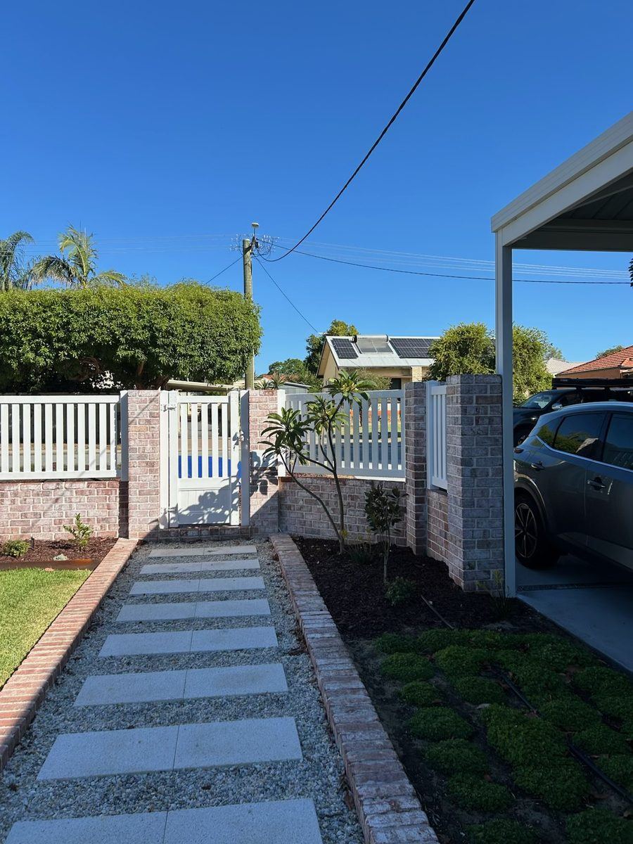 White PVC picket fence between brick piers beside a paved front path