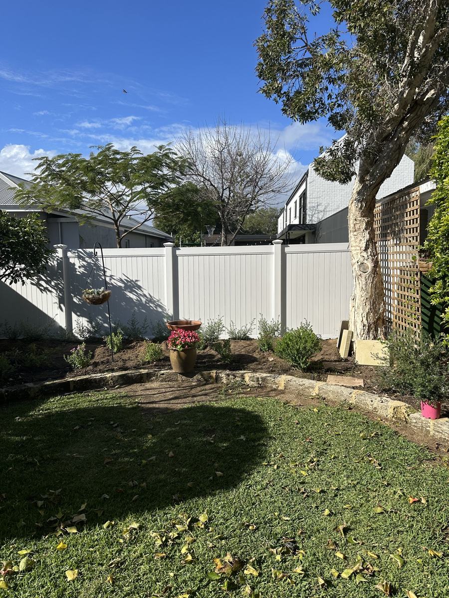 White PVC privacy fence behind a landscaped garden bed and lawn